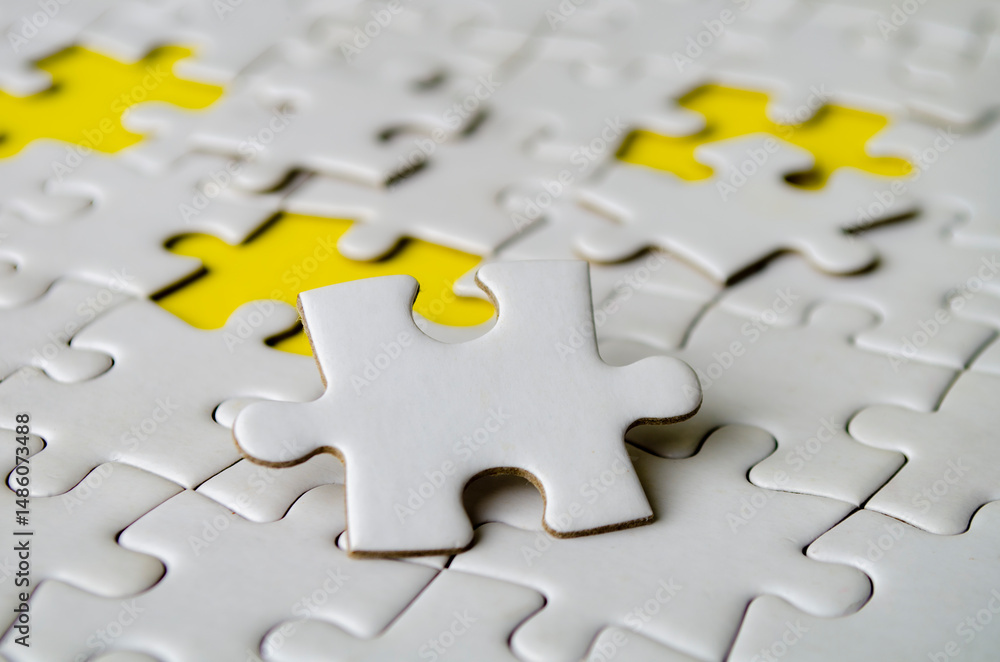 Fototapeta premium Side close up of white jigsaw puzzle pieces placed on a bright yellow background with customizable space on jigsaw for text or ideas.