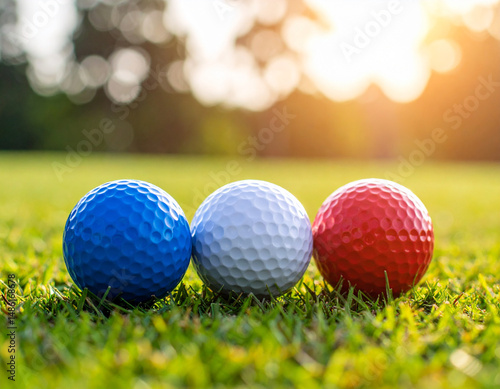 Three colored golf balls, blue, white, and red, are on a green grass field bathed in sunshine