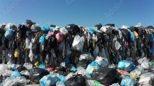 A massive pile of plastic bags and trash against a clear blue sky on a sunny day outdoors