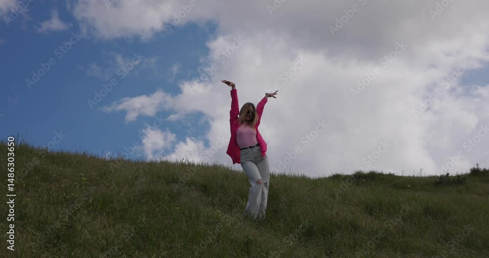 Minimalism, funny girl in pink on a meadow dancing against a clouds background Minimalism, funny girl in pink on a meadow dancing against a clouds background