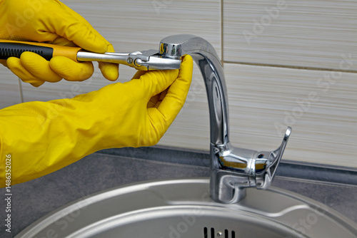 plumber in yellow rubber gloves repairing and servicing a water faucet in a kitchen
