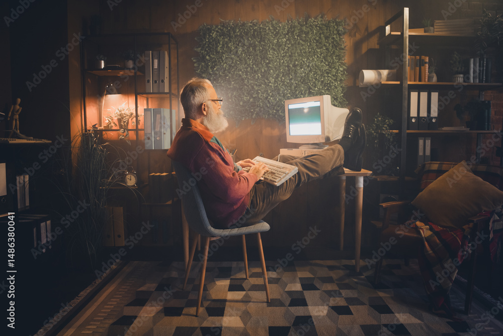 Fototapeta premium Middle-aged man working on an old computer in a cozy home office setting with casual style during the evening