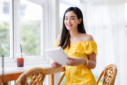 Portrait of beautiful happy Smiling asian woman relaxing sitting in yellow dress at cafe interior in coffee shop background,Business Lifestyle summer holiday concept