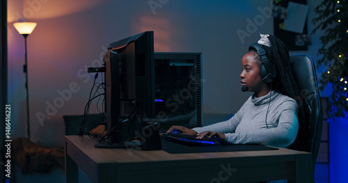 Fotografie A focused young woman plays online multiplayer games with teammates in a dimly lit room