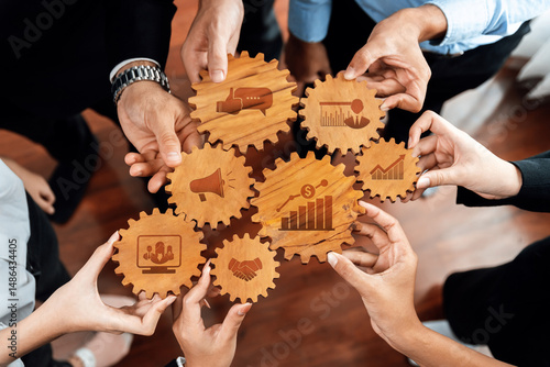 A close-up view of diverse professionals' hands working together, holding wooden gears that symbolize key business concepts like communication, growth, and partnership. Amity
