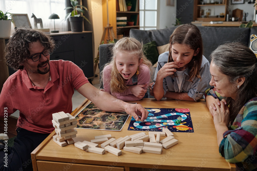 Fototapeta premium Family sitting at table playing board game, with three children and two adults concentrating on the game, socializing and enjoying bonding moment