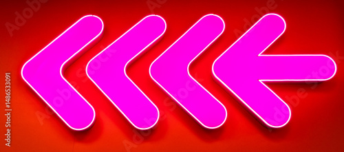 Bright pink neon arrow sign. Glowing neon arrow pointer on the wall of a building