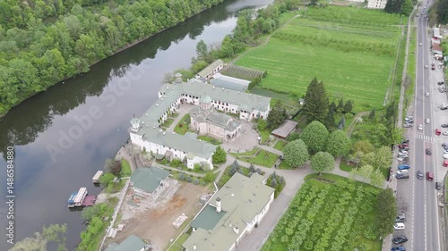 Drone footage capturing a peaceful monastery located at the edge of a flowing river. The aerial view showcases the harmonious blend of sacred architecture and natural surroundings, perfect for religio