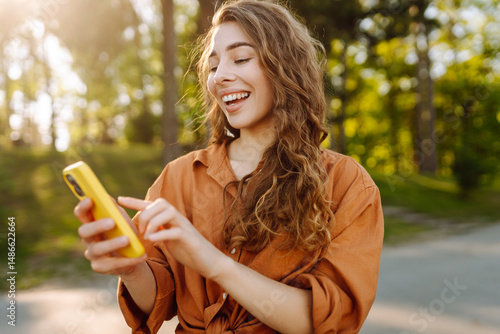 Canvas Print Portrait of cheerful woman with smartphone texting and blogging in sunny park
