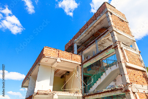 Dilapidated building, its structure exposed against sky. Demolition in progress with exposed concrete and steel beams. Decaying structure of building, revealing internal framework and damage sustained