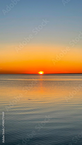 Beautiful sunset over the sea. The sun sets on the water. The sky is painted with bright colors. Summer evening. Sunset beach. Vertical photo.