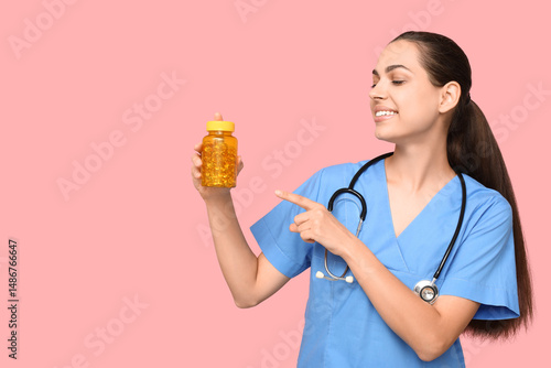 Portrait of female doctor pointing at pills on pink background