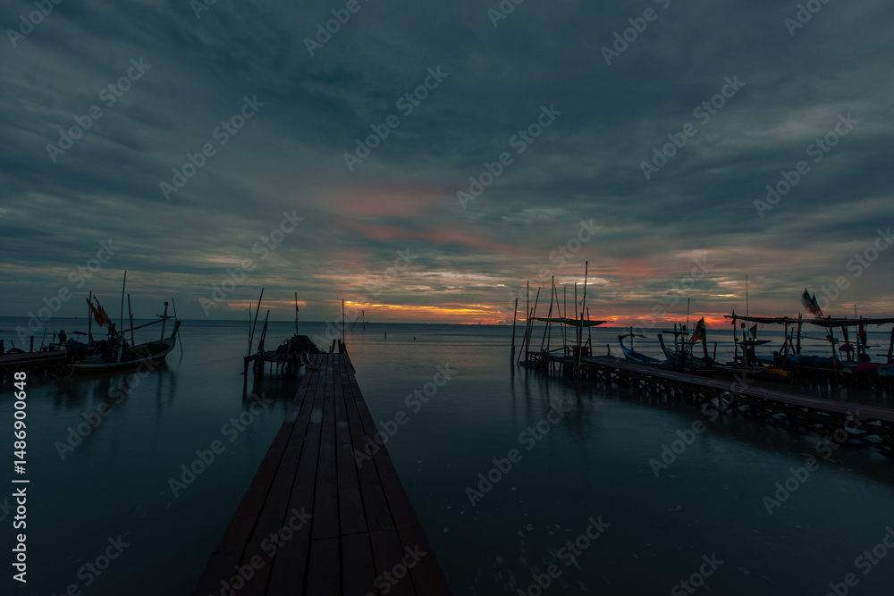 Fototapeta premium Background of golden sunlight in the morning by the sea, with fishing boats moored at the pier, waiting for the time to go out to fish again.
