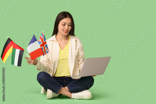 Young Asian woman with flags of different countries and laptop on green backg...