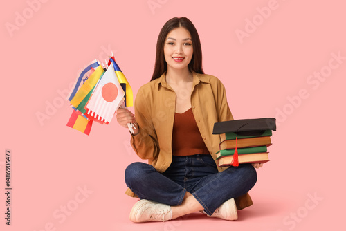 Young Asian woman with flags of different countries and books on pink background