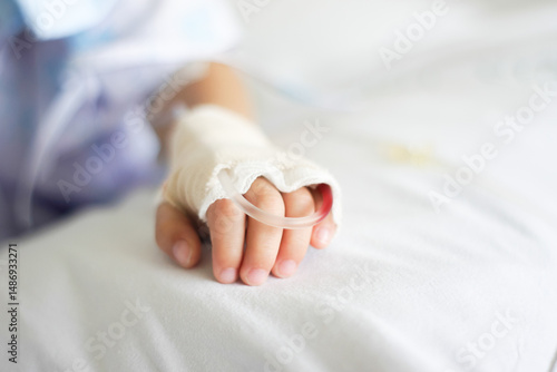 Child's hand with a Saline intravenous (iv) drip resting on a hospital bed, symbolizing medical care, recovery, and compassion in a clinical setting.