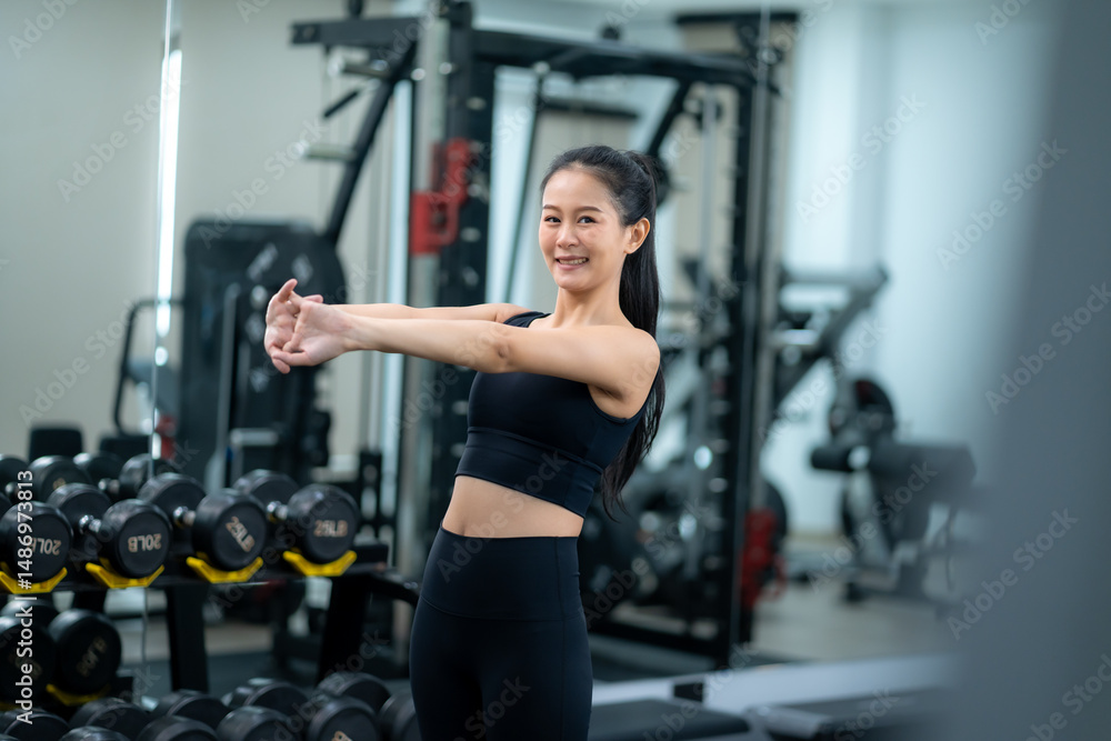 Fototapeta premium Young asian woman stretching her arm before exercise in fitness gym, warming up to prepare her body for workout, healthy and active lifestyle