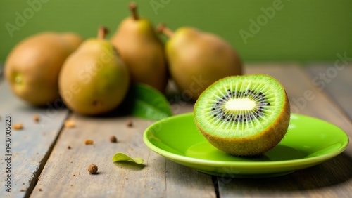 A vibrant half of kiwi fruit rests on a small, bright green plate, surrounded by a blurred background featuring several ripe pears and scattered spices on a rustic wooden surface.