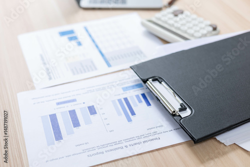 A desk with a laptop, calculator, and a stack of papers. The desk is cluttered and disorganized, with the papers scattered all over the surface
