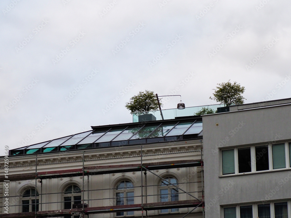 Fototapeta premium Contrast of Historic and Modern Building Architecture with Rooftop Garden Under Cloudy Sky