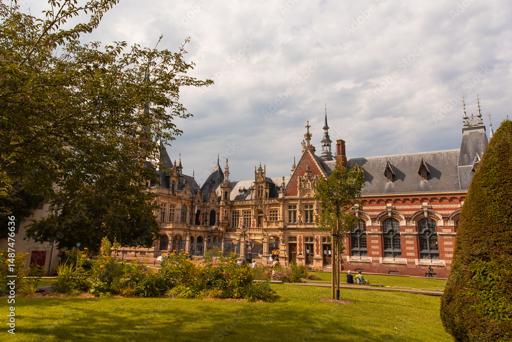 Visitors admire the stunning architecture of Benedictine Palace in France, surrounded by vibrant gardens and lush greenery under a partly cloudy sky. Visitors admire the stunning architecture of Benedictine Palace in France, surrounded by vibrant gardens and lush greenery under a partly cloudy sky.