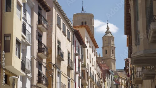 Cinematic gimbal shot moving forward while zooming out along a quiet street in Alcañiz, Aragón, Spain, with a historic bell tower in view