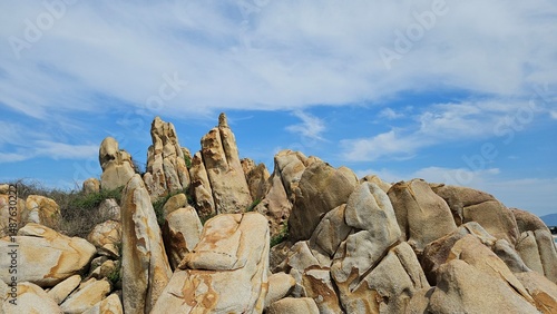 Rock formations rise along the clear shoreline of La Gi town, Vietnam, under a bright blue sky.