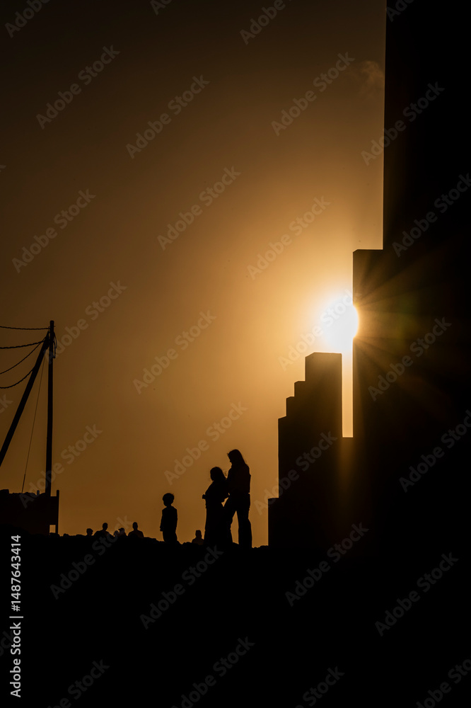 Fototapeta premium A silhouette of a family standing in front of a building. The sun is shining on the building, creating a warm and inviting atmosphere