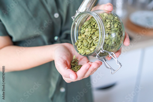 Woman pouring pumpkin seeds from a glass jar they support overall health due to their nutritional properties concept healthy lifestyle, gastronomy, food supplement.