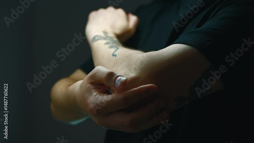 Elbow pain.
Arm fracture and elbow joint injury.
A man in a dark T-shirt is stretching his arm.
The pinched hand of a man in black clothes in a dark room