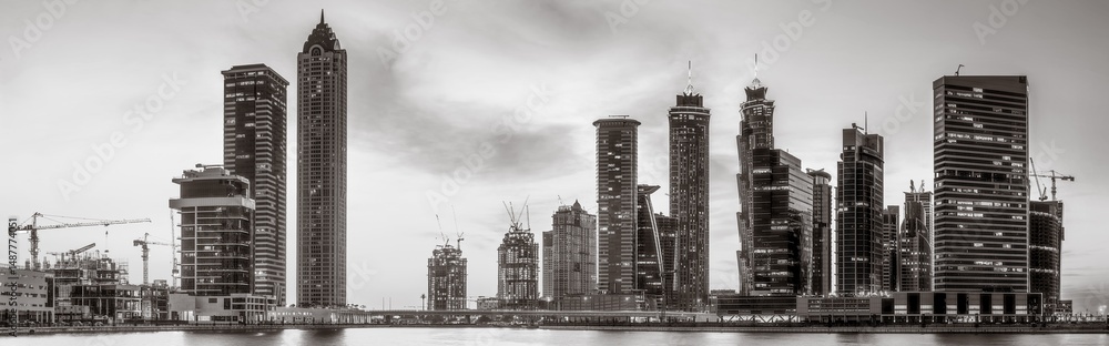 Fototapeta premium Monochrome city skyline with tall skyscrapers reflecting on calm water under a cloudy sky, Dubai Marina bay UAE