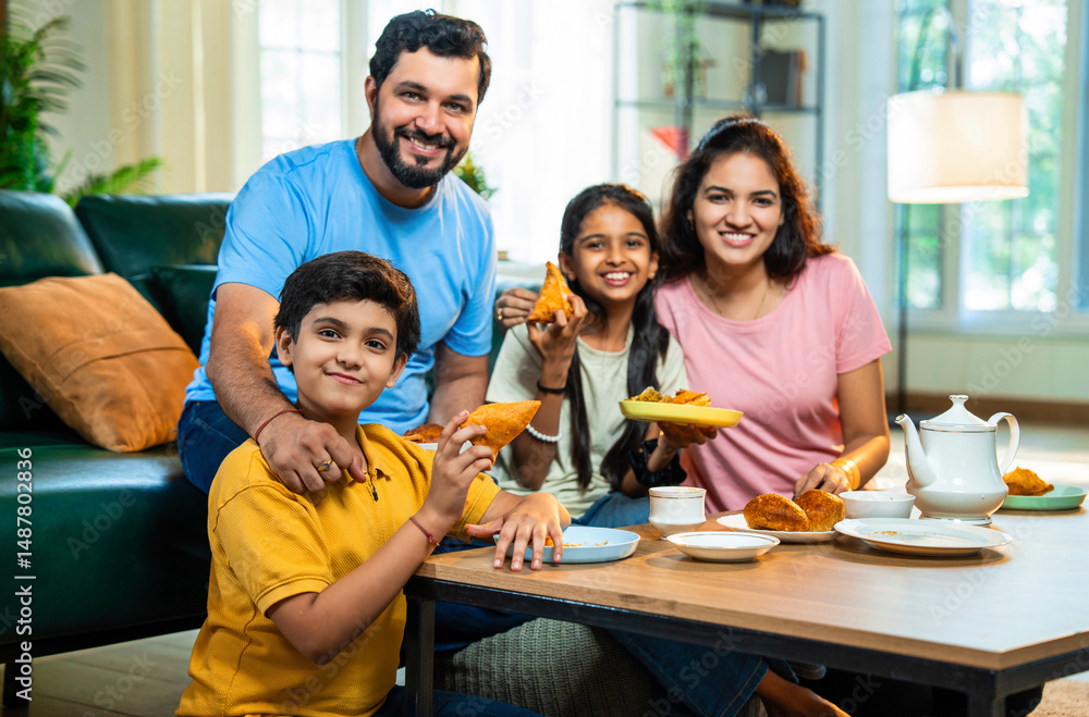 Fototapeta premium Family enjoying evening tea with samosa, sharing laughter and fried snacks in modern living room