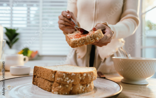 Фотография A woman enjoys a peaceful morning, spreading fresh strawberry jam on bread during breakfast—homemade, healthy, and full of natural sweetness