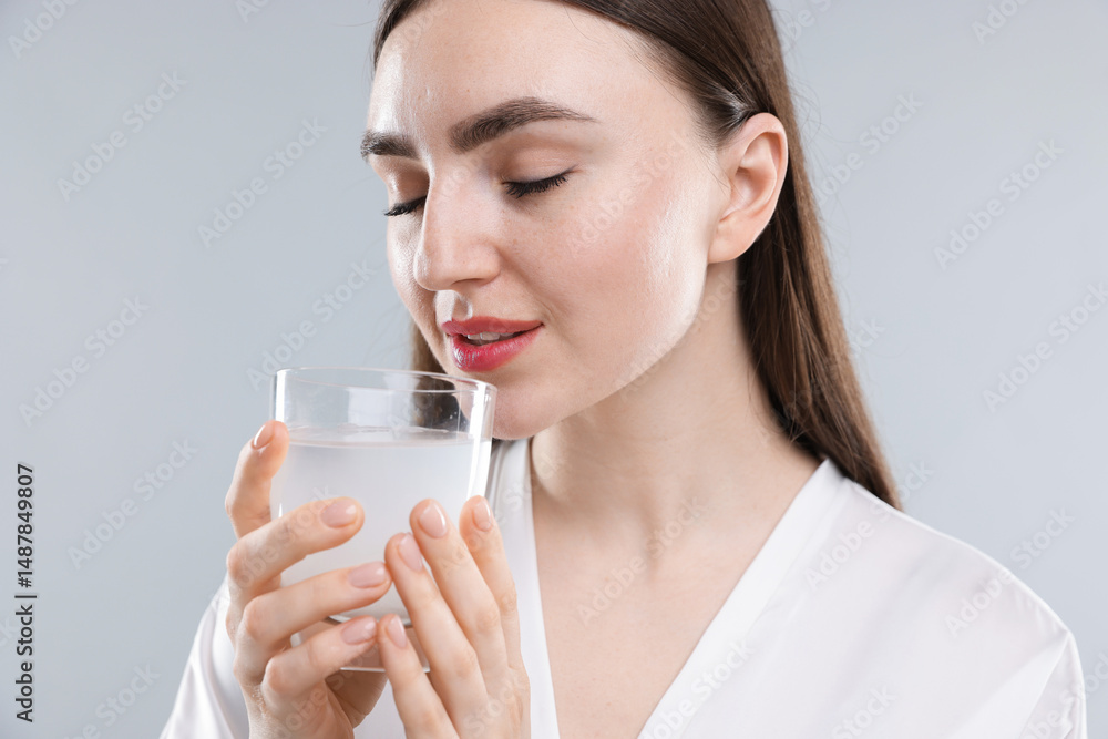 Woman drinking collagen water on grey background Woman drinking collagen water on grey background
