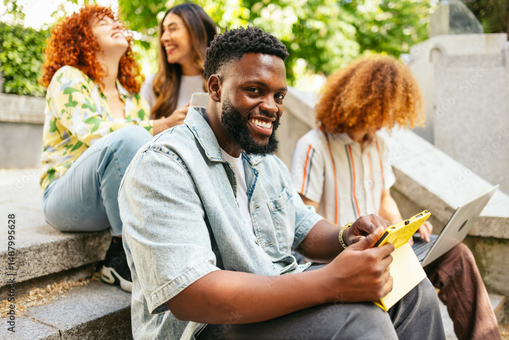 Obraz premium College student using tablet and laptop on campus steps with friends