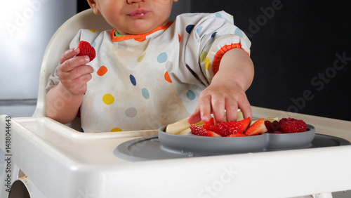 Baby taking a piece of strawberry with his dirty small hand, baby led weaning method