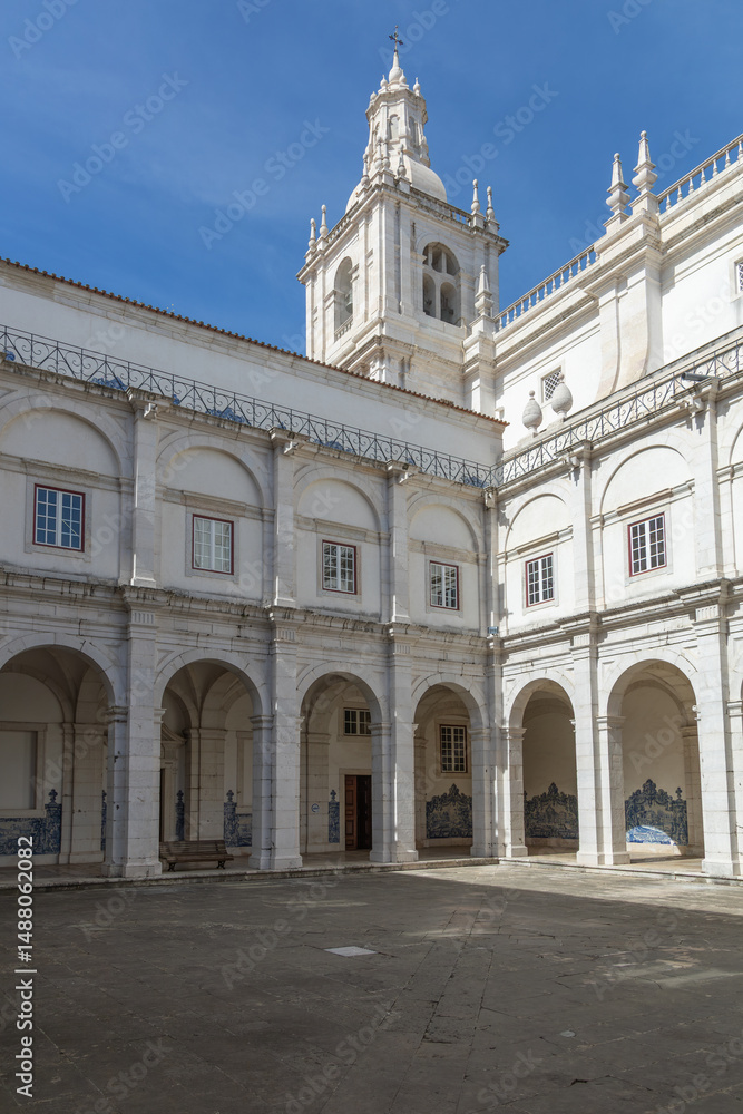Fototapeta premium Beautiful cloister courtyard of São Vicente de Fora historic monastery, featuring arches, blue azulejos tiles, and classical architecture under blue skies. Lisbon, Portugal. 26 February 2025