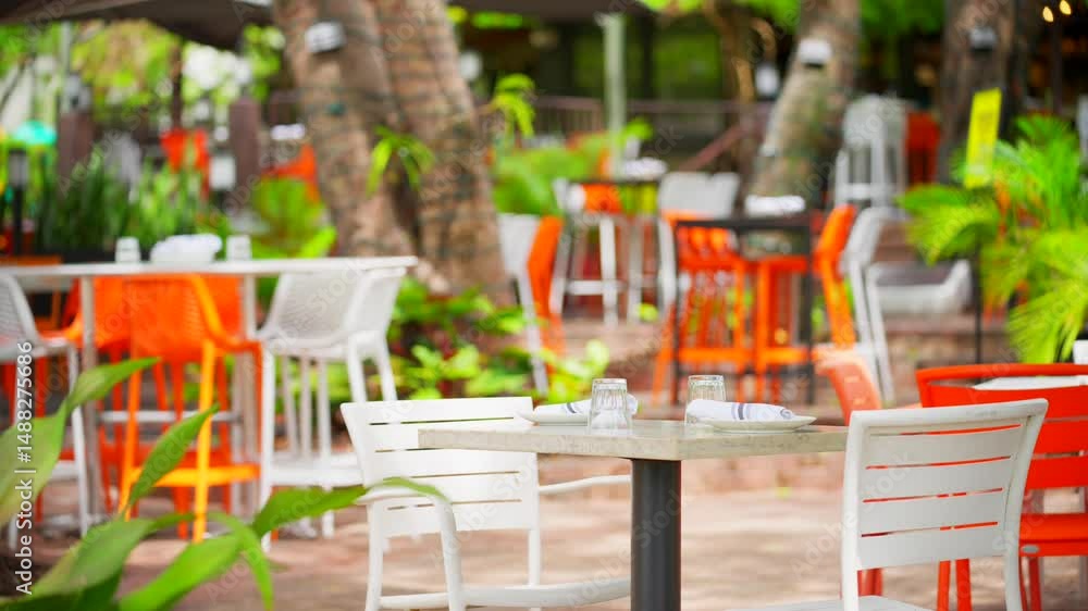 Bright and vibrant outdoor restaurant cafe seating area. Tables chairs and blurry tropical palms in the background Bright and vibrant outdoor restaurant cafe seating area. Tables chairs and blurry tropical palms in the background