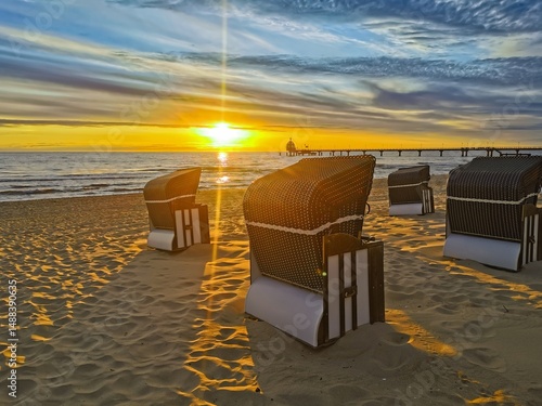 Zinnowitz, Mecklenburg-Vorpommern, Deutschland: Ein malerischer Sonnenaufgang taucht den menschenleeren Strand in goldenes Licht. Strandkörbe stehen ruhig im Sand, die Szene strahlt Freiheit, Ruhe und