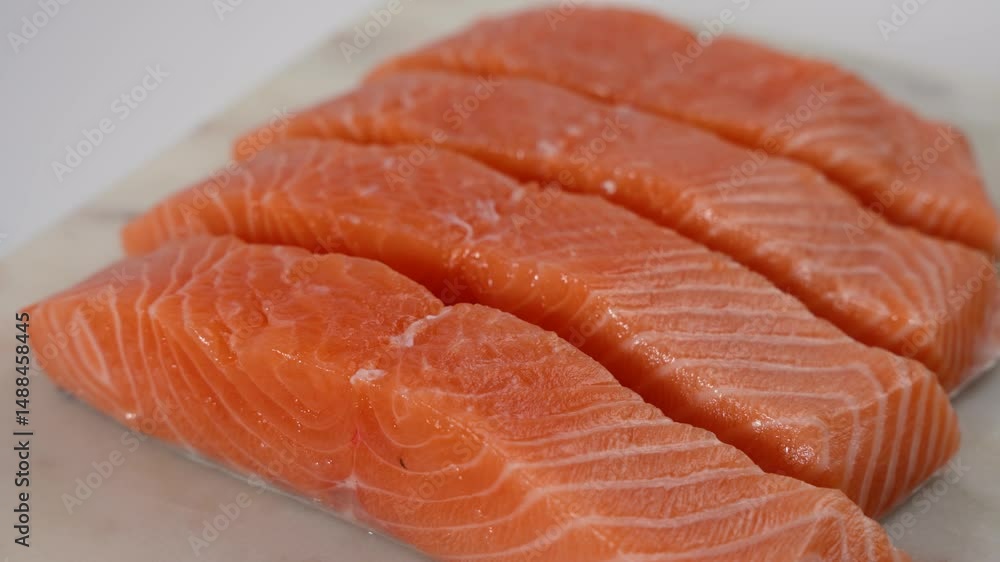 A white cutting board rotates with four pieces of salmon on it. The salmon is cut into four equal pieces, each about the same size. The salmon looks fresh and ready to cook or serve. A white cutting board rotates with four pieces of salmon on it. The salmon is cut into four equal pieces, each about the same size. The salmon looks fresh and ready to cook or serve.