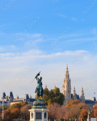 Photography A striking bronze statue stands in the foreground against Vienna's skyline, showcasing architectural beauty with trees adorned in autumn colors under a clear blue sky