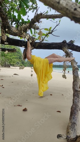Adult beautiful blonde woman walks on the shore of the Andaman Sea and poses under a tree decorated with seashells.