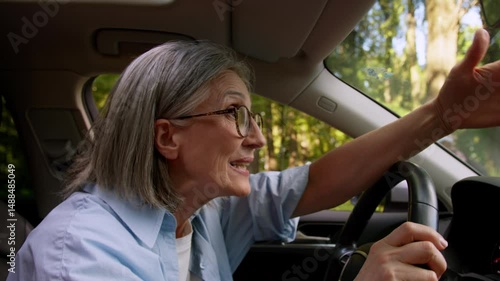Road rage mad furious woman older mature female elderly lady car auto driver riding inside automobile riding vehicle traffic accident yelling shouting gesturing hands aggression rudeness complaining