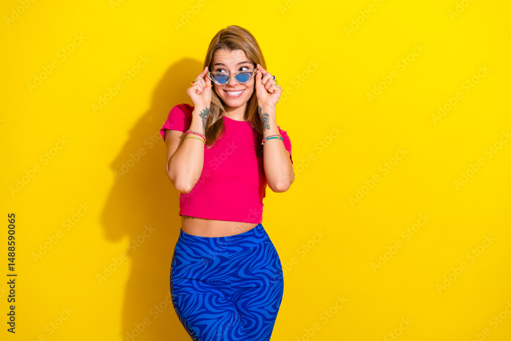 Obraz premium Cheerful young woman in colorful outfit posing against a vibrant yellow background, expressing happiness and charm