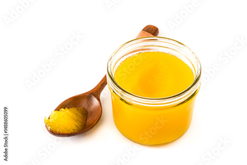 Ghee or clarified butter in open glass jar with wooden spoon presenting product