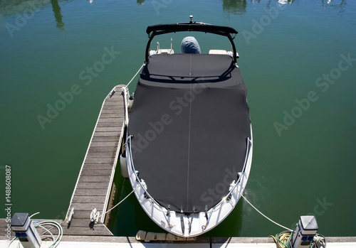 Sleek motorboat covered with black tarp docked at serene marina reflecting calm waters under bright sunlight showcasing peaceful nautical lifestyle