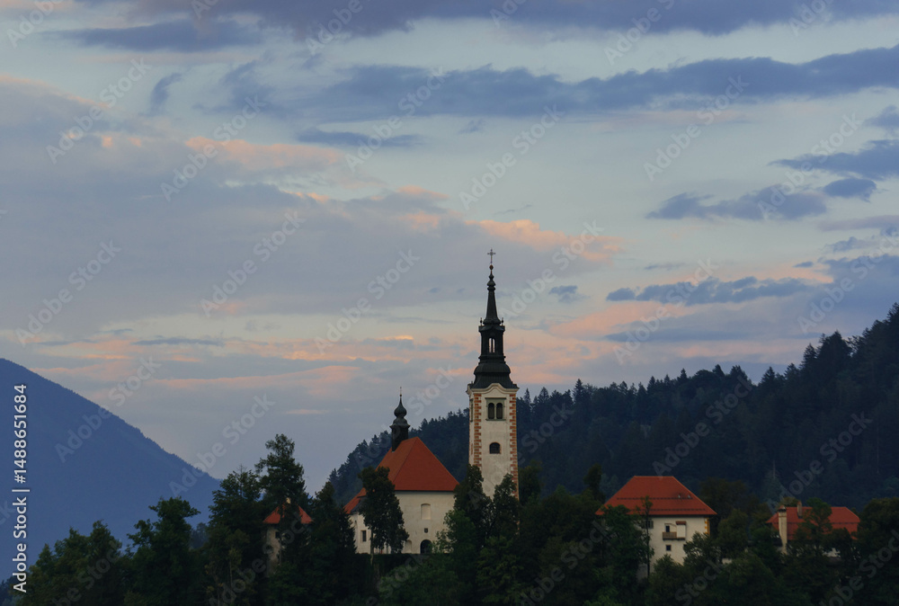 Fototapeta premium very small island on natural bled lake in summer with church in middle and beautiful green trees around with blue waters and clear blue sky