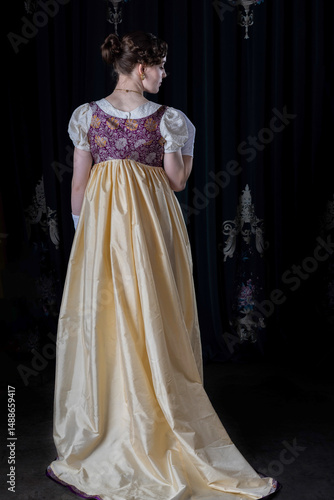 A Regency woman wearing evening attire, including an embroidered dress and a long spencer with gloves