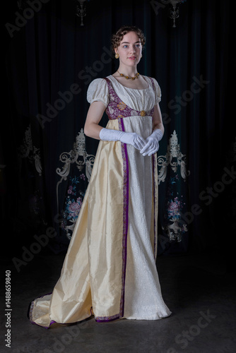 A Regency woman wearing evening attire, including an embroidered dress and a long spencer with gloves