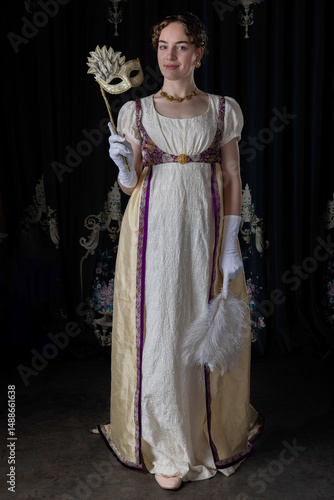 A Regency woman wearing evening attire and holding an ostrich feather fan and a masquerade mask